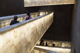 Three of the Museum’s alabaster ramps run in different directions and glow with a soft, yellowish white light. Several people are walking on the two lower ramps.