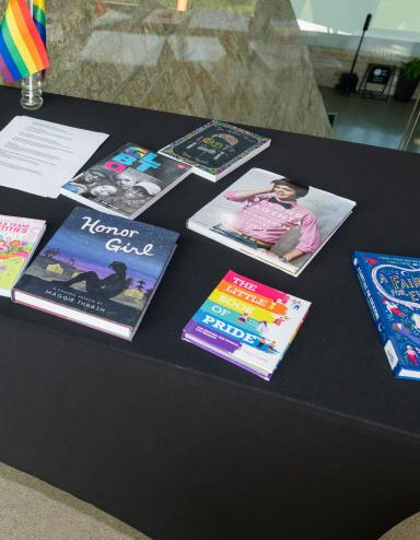 A table with a black tablecloth and colourful books relating to 2SLGBTQI+ Partially obscured.