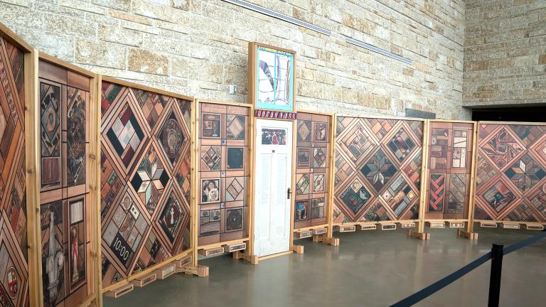 Left view of a structure of vertical wood panels covered in patterns of images, with a white wooden door at the centre.