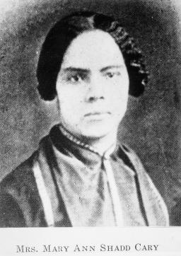 A black and white head and shoulders image of a woman. She is looking directly at the viewer with a serious expression.