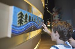 A child touches a painted panel with trees and tipis.