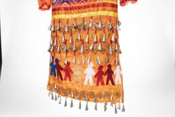 The back side of the orange jingle dress shows eight human figures of various colours all holding hands and standing together in a line which wraps around the dress. Jingles are sewn to the dress above and below the figures.