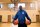 A man stands in a basketball court holding two basketballs. 