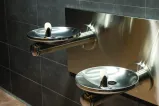 Two water fountains jut out of a wall. They are located side-by-side, but one fountain is set lower than the other.