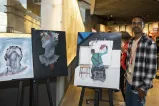 In a museum gallery, a student stands beside three paintings that they've created.
