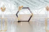 A wedding ceremony set-up with clear chairs and an arch with flowers on it.