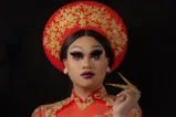 A drag artist is wearing Vietnamese cultural clothing with a matching red and gold headdress and long dress.