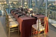 Nestled in a corner of the observation platform of the glass tower is a lavishly decorated table with burgundy tablecloth, floral arrangements and dinnerware, and gold chairs.