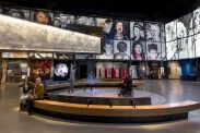 Five people in a museum gallery. Two sit on a bench. Three people, including one in a wheelchair, are on a circular area where bubbles of coloured light are projected on the floor.