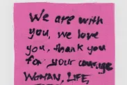 Piece of cloth with "We are with you, We love you, Thank you for your courage Woman, Life, Freedom" written with a black marker.