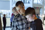 An adult man and a teenaged boy stand beside one another looking down at an interactive table.