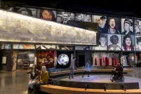 Five people in a Museum gallery. Two sit on a bench. Three people, including one in a wheelchair, are on a circular area where bubbles of coloured light are projected on the floor.