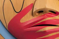 A closeup of a carved wooden box, showing a painted image of a red hand over a carved mouth.