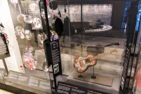 A row of museum display cases with various artifacts inside. A guitar is displayed under glass. The guitar has a colourful floral print with a bird hand-painted onto its front.
