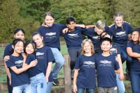 A group of youth outside on a wood fence, posing for the camera with their arms around one another. 