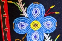 A blue beaded flower on a black and red background. 