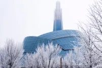 An unusual building surrounded by a glass "cloud" and topped by a tower. It is surrounded by snow and bare trees.
