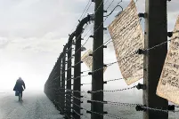 A person walking by a barbed-wire fence. Sheet music is caught in the wire.