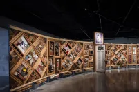 A large horizontal art installation with a wooden frame made up of multiple diamonds and rectangles to which many objects are mounted. There is a half-opened door in the middle of the work.