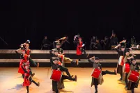 A drumming troupe dancing on a stage. The drums and parts of their costumes are a bright red.