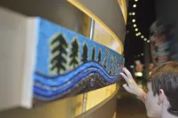 A child touches a painted panel with trees and tipis.