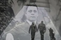 A translucent historical image of a man in a suit layered over a contemporary photo showing the dark outline of two men walking in a hallway.