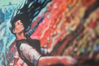 A black-haired woman appears to be in an abstract, colourful windstorm with red and blue.