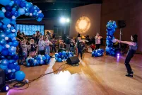 Kids dancing in a hall filled with blue balloons.