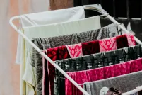 Garments are hung over a rack to air dry. The fabrics are grey, black, white and shocking pink.