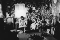 A black and white image of women and young children sitting on couches and chairs in a small living room.