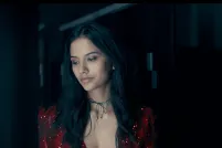 A woman with long dark hair and a red dress is pictured from the waist-up, looking downward towards something off screen. Another woman's face can be seen on the other side of the frame, looking in the same direction.