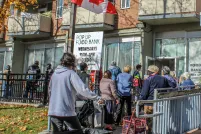 A line-up of people wait outside a building. There are signs indicating it is a Food Bank. A Canadian flag flies above them.