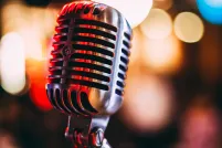 A performance microphone in the foreground reflects red and gold lights. Blurred in the background are patio lights.