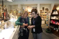Two women look at a piece of jewellery. They are standing in a store full of colourful merchandise.