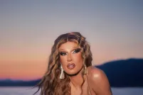 A person with long blond crimped hair sitting on a ledge overlooking a large body of water in a gold bikini.