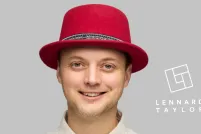 A smiling green-eyed man wears a red felt top hat and an ivory collared shirt with black snaps.