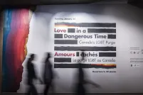 Three silhouettes of people walking past a large wall panel featuring the logo for the Love in a Dangerous Time exhibition. The silhouettes are blurred as the individuals are walking from left to right.
