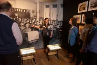 A visitor looks at a gallery niche on residential schools at the Canadian Museum for Human Rights. Two small desks sit in the middle of the niche. A large image of Indigenous students sitting at desks at a residential school is on the back wall of the niche, with images and artifacts on the side walls.