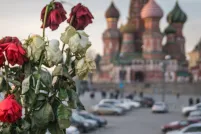 Des roses rouges et blanches fanées dans un vase. En arrière-plan, on voit la cathédrale Saint-Basile sur la place Rouge, à Moscou, avec ses multiples coupoles et dômes, qui rappellent un feu de camp montant vers le ciel.