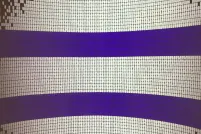 An image being projected onto a curved wall that is about nine feet tall. It is made up of many small squares and has the appearance of Indigenous bead work or a mosaic. The image is mainly made up of white squares, but it also features two thick blue horizontal lines that run parallel to each other.