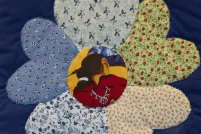 Close-up of a flower on a quilt. Each of the petals is a different flowery fabric, while at the centre of the flower is fabric onto which is printed the face of an Indigenous woman in profile.
