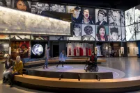 Five people in a museum gallery. Two sit on a bench. Three people, including one in a wheelchair, are on a circular area where bubbles of coloured light are projected on the floor.