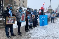  A line of people holding photographs and signs stand outside government buildings.