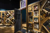 A large, free-standing art installation contains hundreds of objects. It is framed in cedar and there is an open door in the middle that people can walk through.