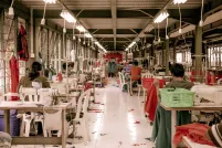 Garment workers sit at desks with sewing machines in a warehouse.