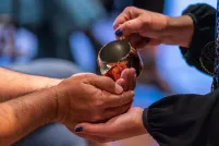 A person pours water from a copper cup into the cupped hands of another person.