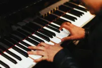 Two hands play the keys of a gleaming black Yamaha piano. The pianist, barely shown, wears a long-sleeved black top.