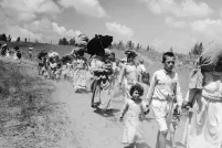 Women and children carrying bundles on their heads walk along a dirt road.