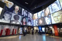 The museum's Canadian Journeys gallery, seen from the perspective of a visitor standing in the middle of it, surrounded by niches that share stories of Canadian experiences of human rights. On the walls above the niches, large images of faces of Canadian human rights defenders are seen arranged in a grid pattern.