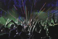A digital illustration showing a crowd clapping and raising their hands. The background shows a pixelated green soundwave shape and blue and black graffiti-like designs with neon-coloured diagonal lines radiating out from the center.